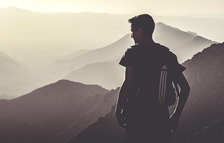 man with back turned to camera looking at scenic view of mountain range